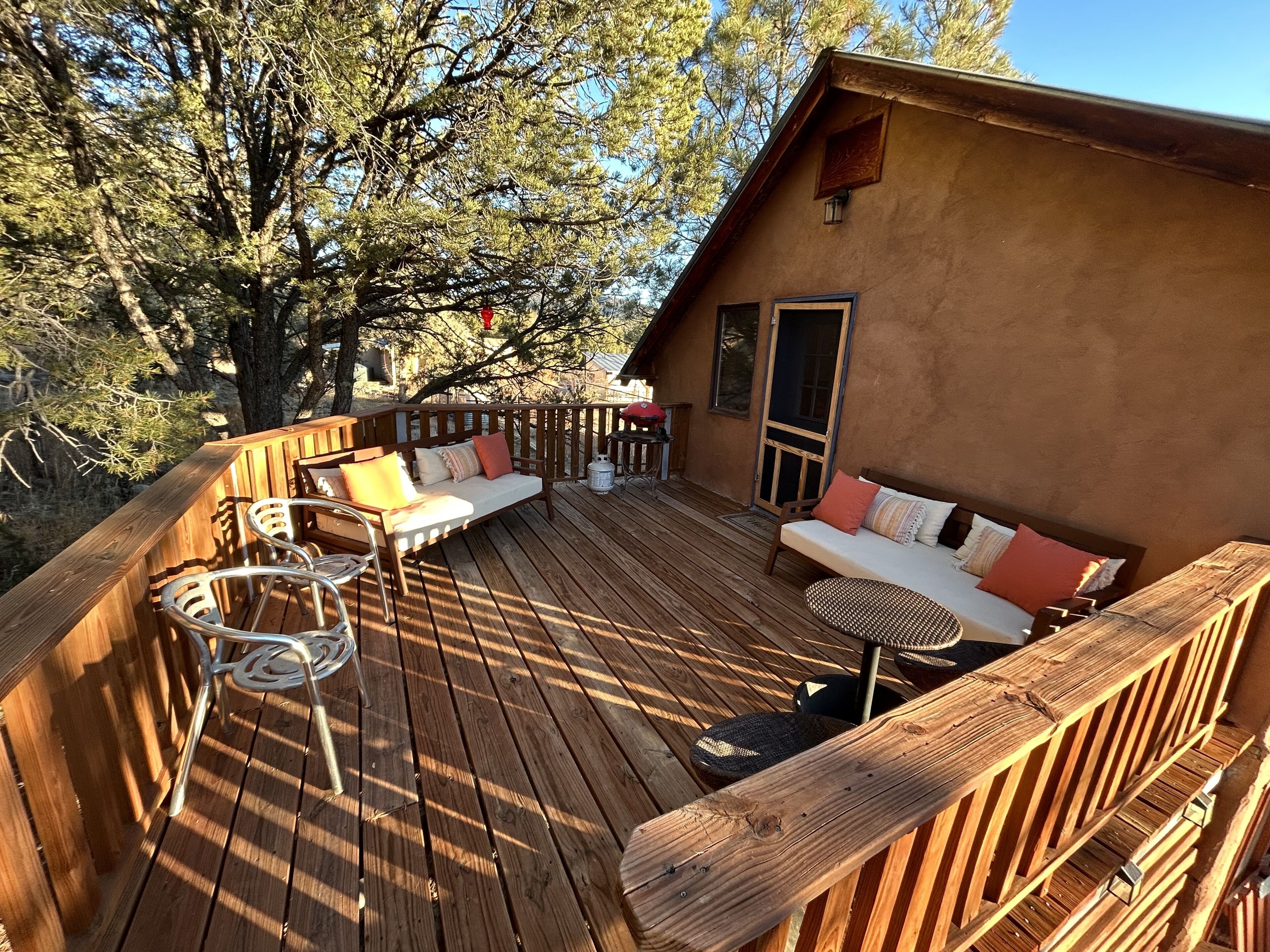 Un terrazzo in legno con un divano, sedie, un barbecue e una porta che dà sull'interno.