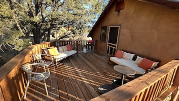 Un terrazzo in legno con un divano, sedie, un barbecue e una porta che dà sull'interno.
