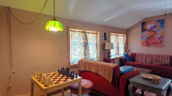 Una sala de estar acogedora con un tablero de ajedrez, un sofá rojo, un plaid estampado y un cuadro en la pared.