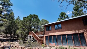 A two-story building with a wooden deck and a large windowed room. - Artist Retreat~Forest Getaway~Adventurers~Hunters~Writers~Nature Lovers (El Rito)
