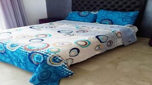 Una cama con colcha estampada y almohadas a juego, un cabecero acolchado y una mesita de noche con lámpara.