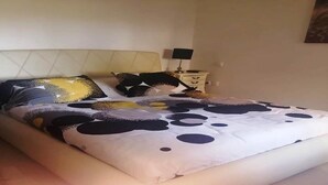 Una cama bien hecha con una colcha estampada, una mesita de noche con una lámpara y una pared con un cuadro.