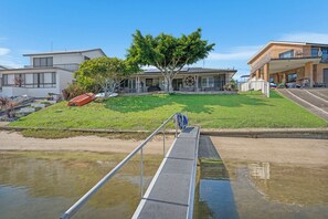 Un edificio moderno con techo plano, un árbol en primer plano y un pasarela metálico sobre el agua.