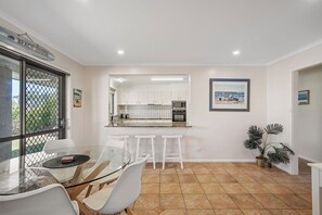 Cocina moderna con armarios blancos, una mesa de comedor de vidrio y vista a la playa a través de un ventanal grande.