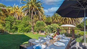 Un espace de restauration en plein air avec une table dressée pour quatre personnes, entouré d’une végétation luxuriante et de palmiers.