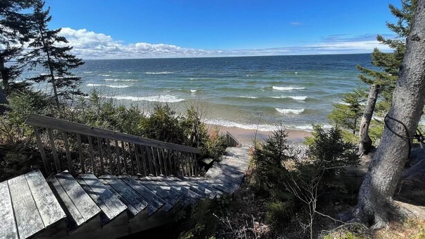 Eine Holztreppe führt zu einem Strand mit Blick auf das Meer.