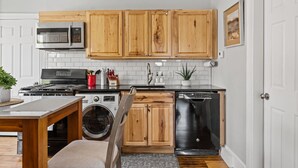 Una cocina compacta con armarios de madera, microondas, lavavajillas y lavadora.