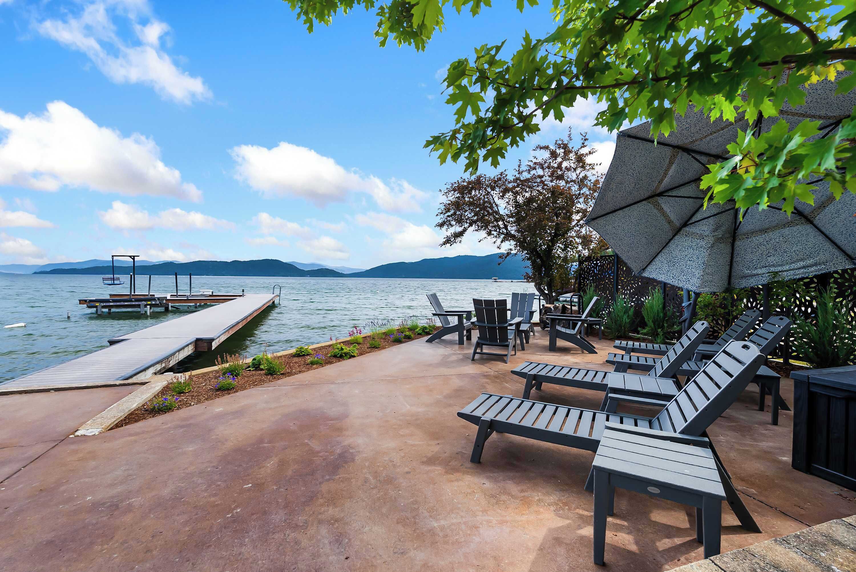 Une terrasse au bord de l’eau, dotée de chaises longues, d’un quai et d’un grand parasol.