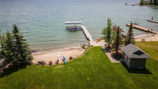 A lakeside property with a dock, a small cabin, and a grassy area with outdoor seating. - Dog-Friendly Beachfront Getaway, Hot Tub, Boat Lift (Sandpoint)