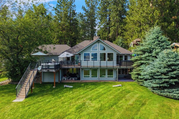 A two-story house with a covered patio, a staircase, and a large lawn.