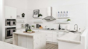 Et moderne køkken med hvide skabe, en central ø, indbyggede ovne og et rustfrit stål emfang.