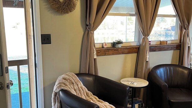 A living room with a black leather sofa, a small round table, and a coffee table. A door with a glass panel leads to an outdoor area.