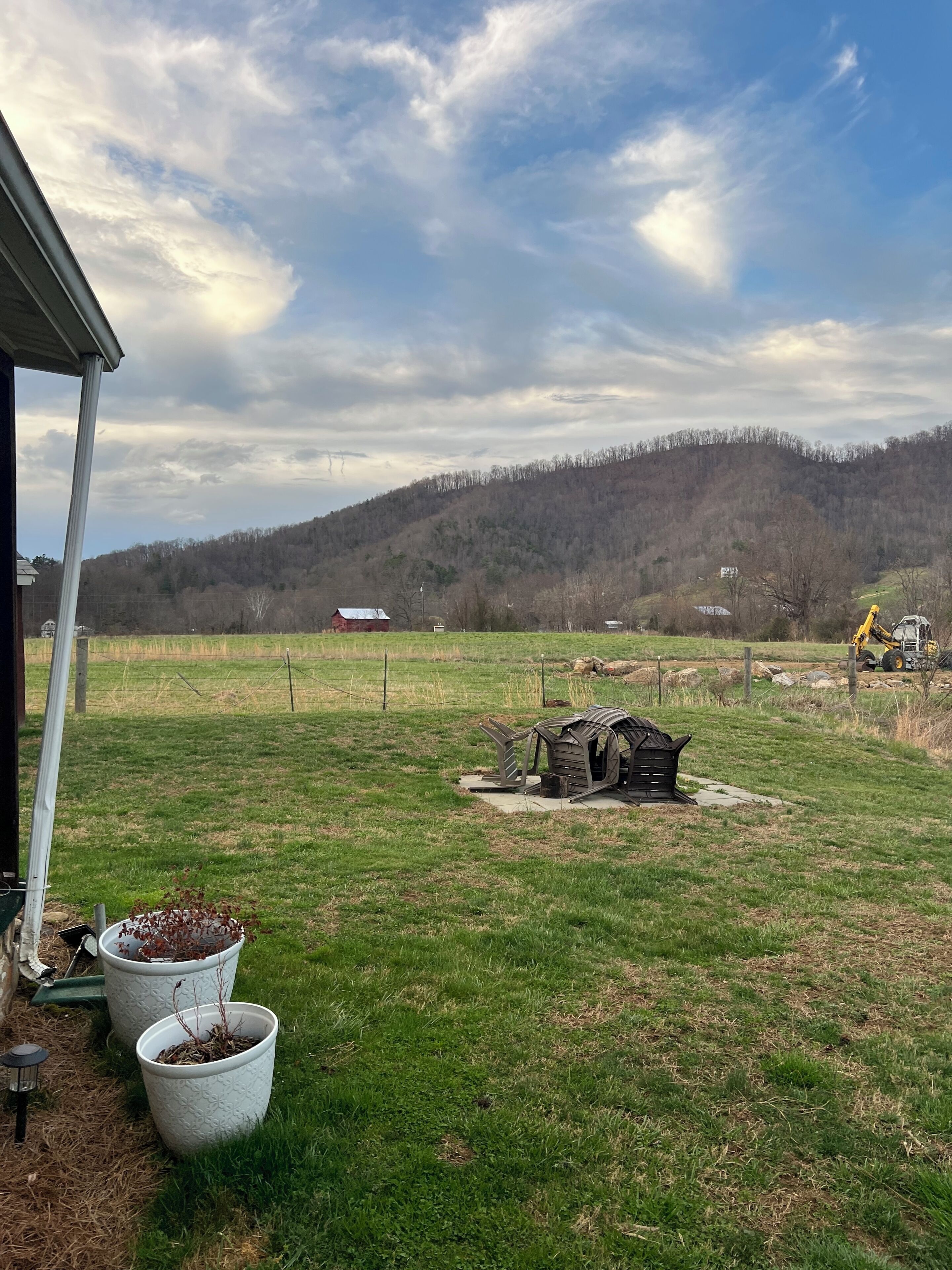 A rural landscape with a grassy field, a wooden structure, and a distant hill.