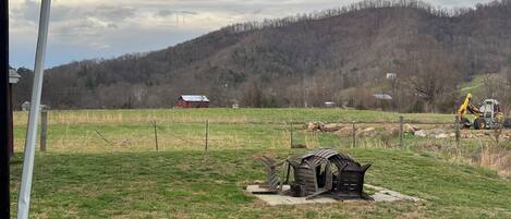 A rural landscape with a grassy field, a wooden structure, and a distant hill.