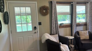 A living room with a door, two windows with curtains, a fireplace, and a black leather sofa.