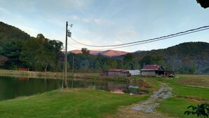 A rural landscape with a pond, a wooden barn, and a mountain in the background.