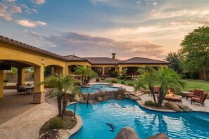 A pool area with a stone patio, lounge chairs, and a building with arches. - Pet Friendly, Extravagant North Scottsdale Estate - Theater, Bball & more! (Cave Creek)