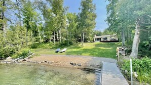 Una propiedad junto al lago con un muelle de madera, un área verde y una casa al fondo.
