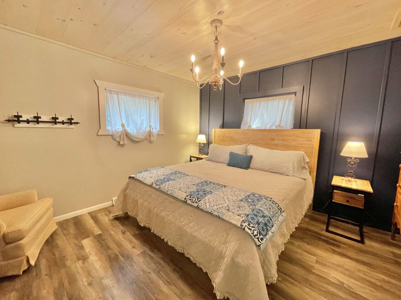 Ein Schlafzimmer mit einem großen Bett, zwei Nachttischen, einer Chandelüster und einem fenster mit Vorhängen.