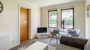 Un saló amb televisió, taula de vidre, dues cadires, sofà i una porta.