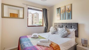 Habitació d'hotel amb un llit gran, una finestra amb cortines, una tauleta de nit amb una làmpada i obra d'art a la paret.