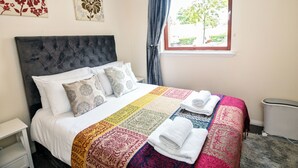 A neatly made bed with a colorful quilt, a window with a view of greenery, and a radiator on the floor. - 2 Bed Flat - Sleeps 4 - Parking - Wifi (Aberdeen)