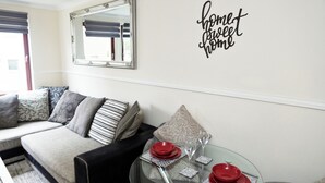 A living room with a sofa, a glass coffee table, and a wall with a 'home sweet home' sign. - 2 Bed Flat - Sleeps 4 - Parking - Wifi (Aberdeen)