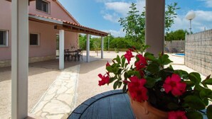 A covered patio area with a stone pathway, outdoor furniture, and a potted plant with red flowers. - Vacation home Nina by Interhome (Šibenik/Dubrava)