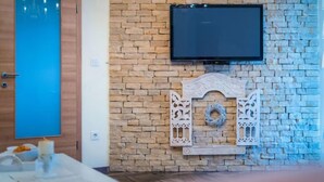 A room with a stone wall, a mounted TV, and a decorative fireplace. - Vacation home Nina by Interhome (Šibenik/Dubrava)