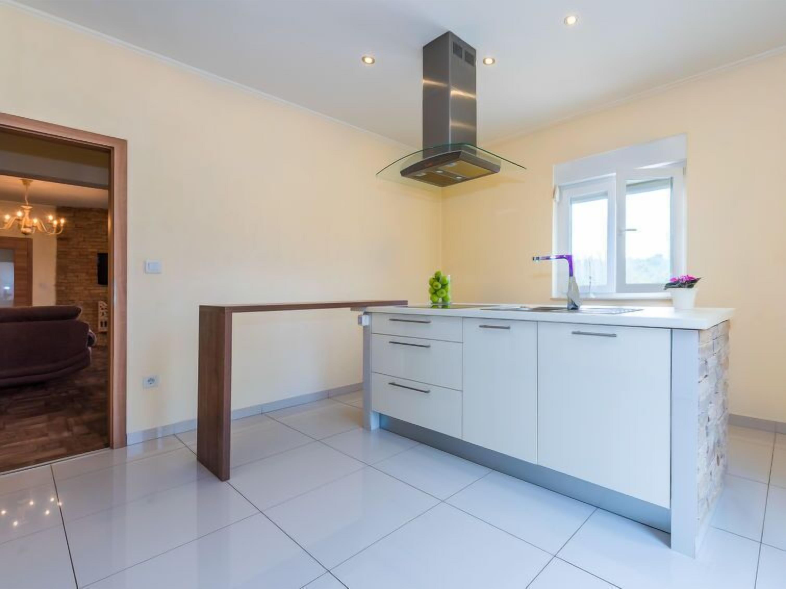 A modern kitchen with white cabinetry, a stainless steel range hood, and a window providing natural light.