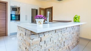 A modern kitchen with a central island, built-in appliances, and a stone accent wall. - Vacation home Nina by Interhome (Šibenik/Dubrava)