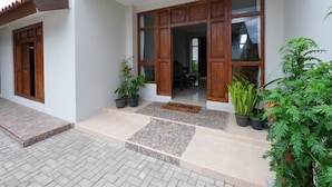 A building entrance with a tiled porch, wooden doors, and potted plants. - OYO 3906 Dalem Putu Sanjaya Syariah (Sleman)