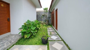 A narrow corridor with a stone pathway, green grass, and potted plants. - OYO 3906 Dalem Putu Sanjaya Syariah (Sleman)