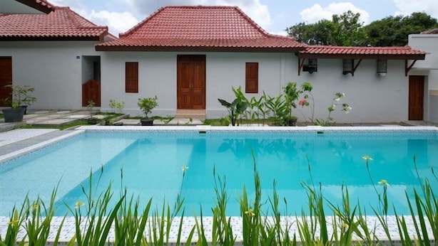 A swimming pool with a tiled deck, surrounded by a white building with red-tiled roofs and wooden doors. - OYO 3906 Dalem Putu Sanjaya Syariah (Sleman)