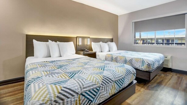 A hotel room with two beds, a large window, and a view of the outside.