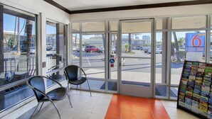 A hotel lobby with large glass doors, a seating area with chairs, and a display of local attractions.