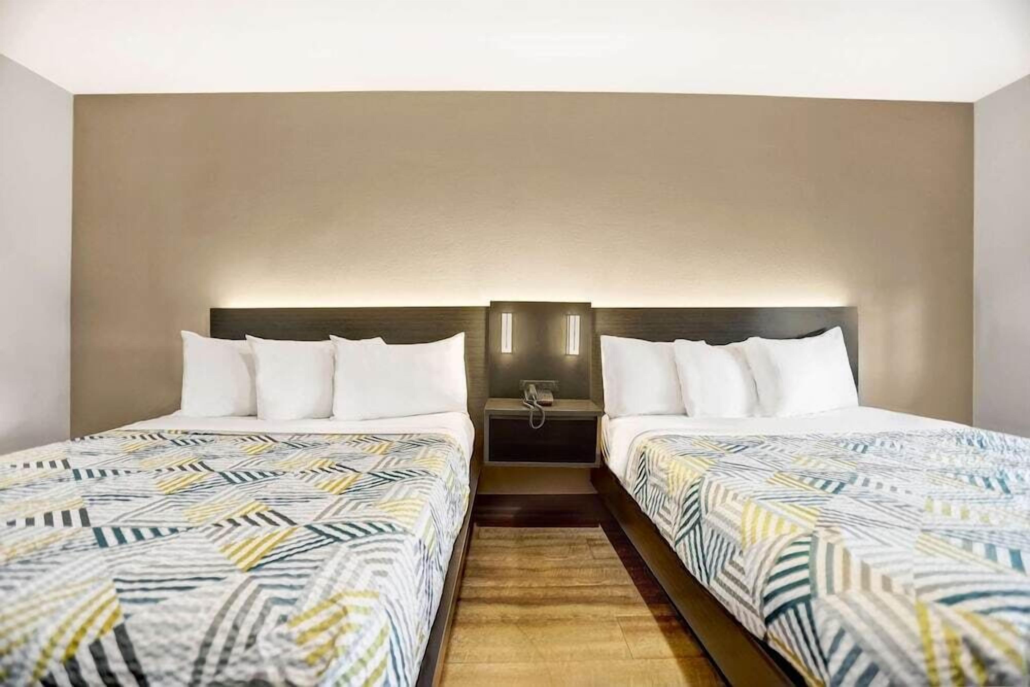 A hotel room with two beds, a headboard with integrated lighting, and a small bedside table with a phone.