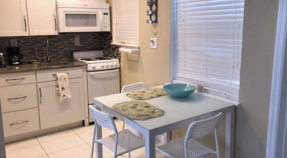 A compact kitchen with white cabinets, a microwave, a stove, and a table with chairs.