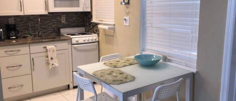 A compact kitchen with white cabinets, a microwave, a stove, and a table with chairs.