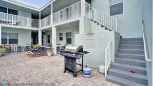 Ein zweistöckiges Gebäude mit überdachter Terrasse, Grill und Treppe.