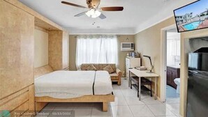 Ein Schlafzimmer mit Bett, Schreibtisch, Deckenventilator und Fernseher.