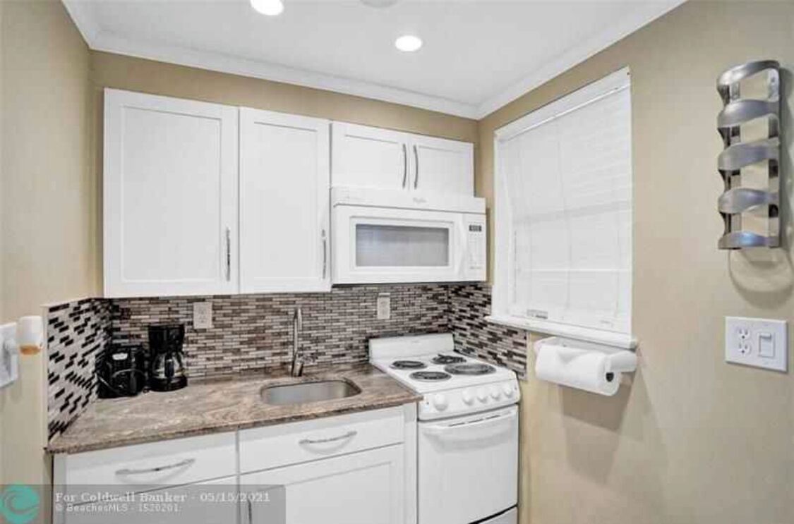 A compact kitchen with white cabinets, a microwave, a stove, and a sink.