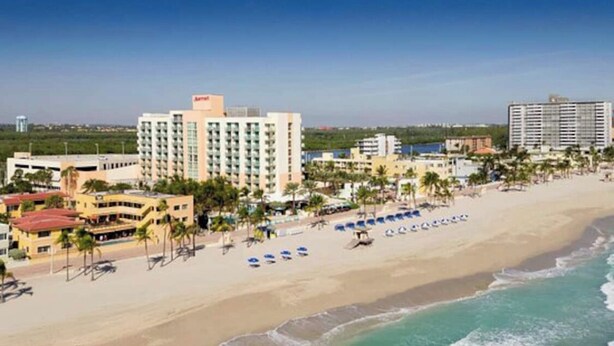 Ein Strandhotel mit mehreren Gebäuden, einem Sandstrand und Palmen.