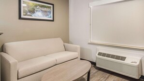 A room with a beige sofa, a small round table, a wall-mounted projector screen, and a white air conditioning unit. - Quality Inn & Suites Fort Worth - Fossil Creek (Fort Worth)