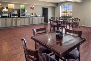 Un grand espace à manger avec une table et des chaises en bois, un coin cuisine équipé d’appareils électroménagers et d’un réfrigérateur, ainsi qu’une grande fenêtre offrant une vue dégagée.