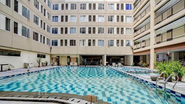 Un edificio de varios pisos con un área de piscina central que presenta un diseño a cuadros.