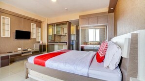 Una habitación de hotel moderna con una cama grande, un televisor de pantalla plana, un minibar y un baño con cabina de ducha de vidrio.