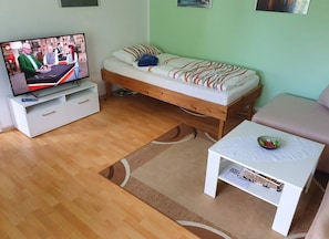 A room with a bed, a TV, a white table with a bowl, and a sofa.