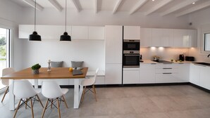 A modern kitchen with white cabinetry, a wooden dining table, and pendant lighting. - High-end Luxury Apartment & Convenient Location (Tsoukalades)