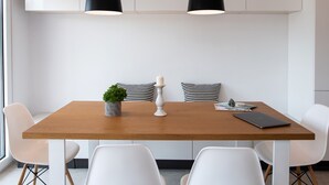 A modern dining area with a wooden table, white chairs, black pendant lights, and a small potted plant. - High-end Luxury Apartment & Convenient Location (Tsoukalades)